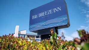 A large sign for Bay Breeze Inn with a modern design and a view of the building in the background.