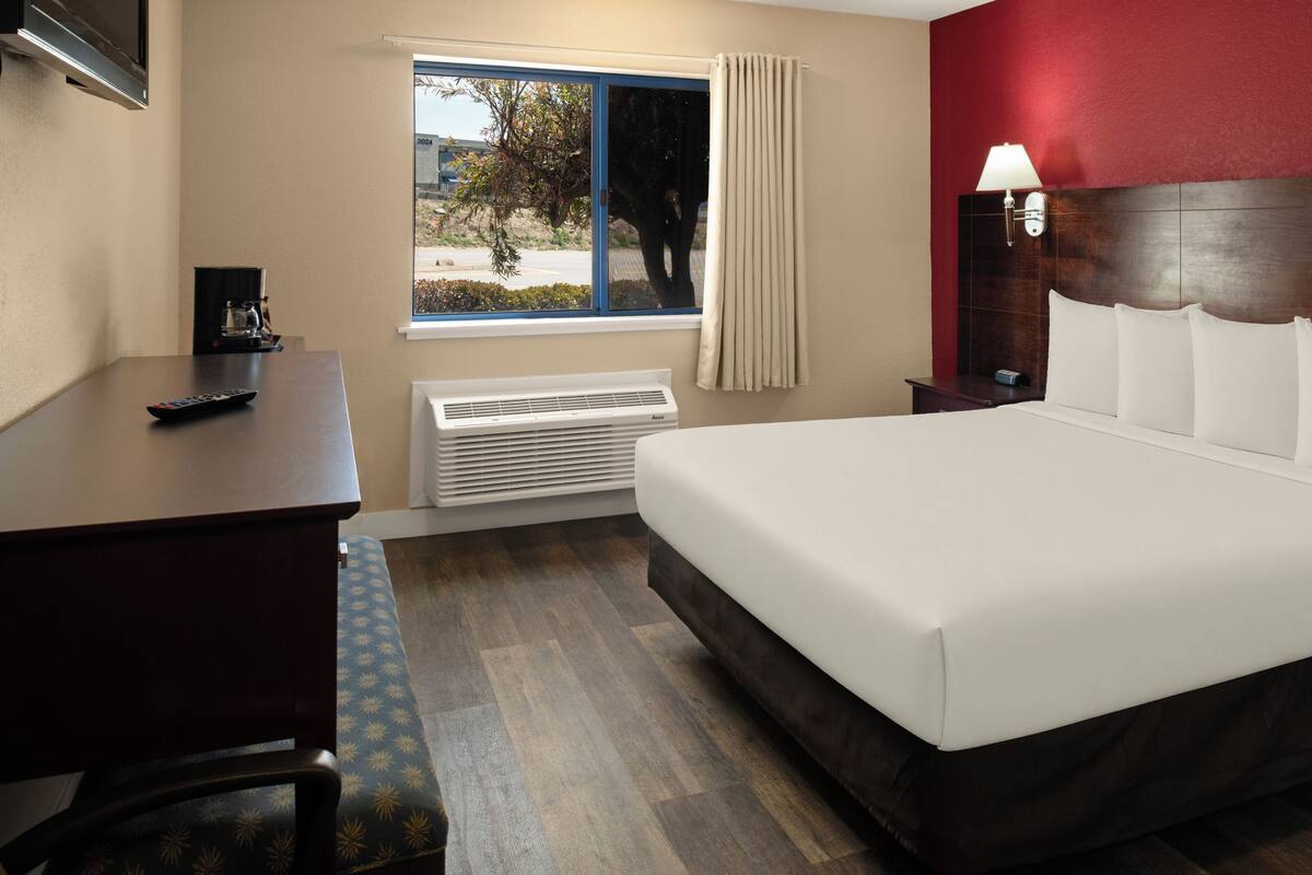 Una habitación de hotel con cama, escritorio, silla, ventana con vistas, mesita de noche y lámpara.