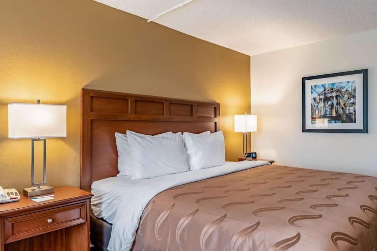 A hotel room with a wooden headboard, a bed with a patterned bedspread, two bedside lamps, a nightstand with a telephone, and a framed picture on the wall.