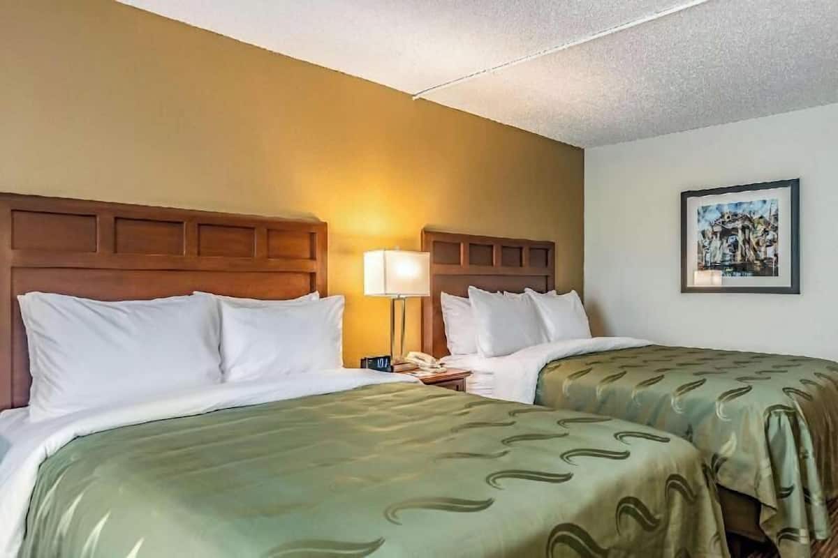 A hotel room with two beds, a headboard, a bedside lamp, a framed picture on the wall, and a telephone on the nightstand.