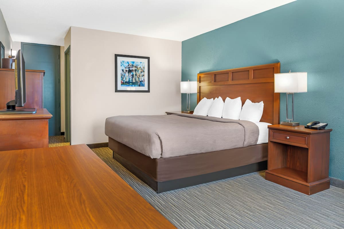A hotel room with a bed, bedside tables, a desk, and a framed picture on the wall.