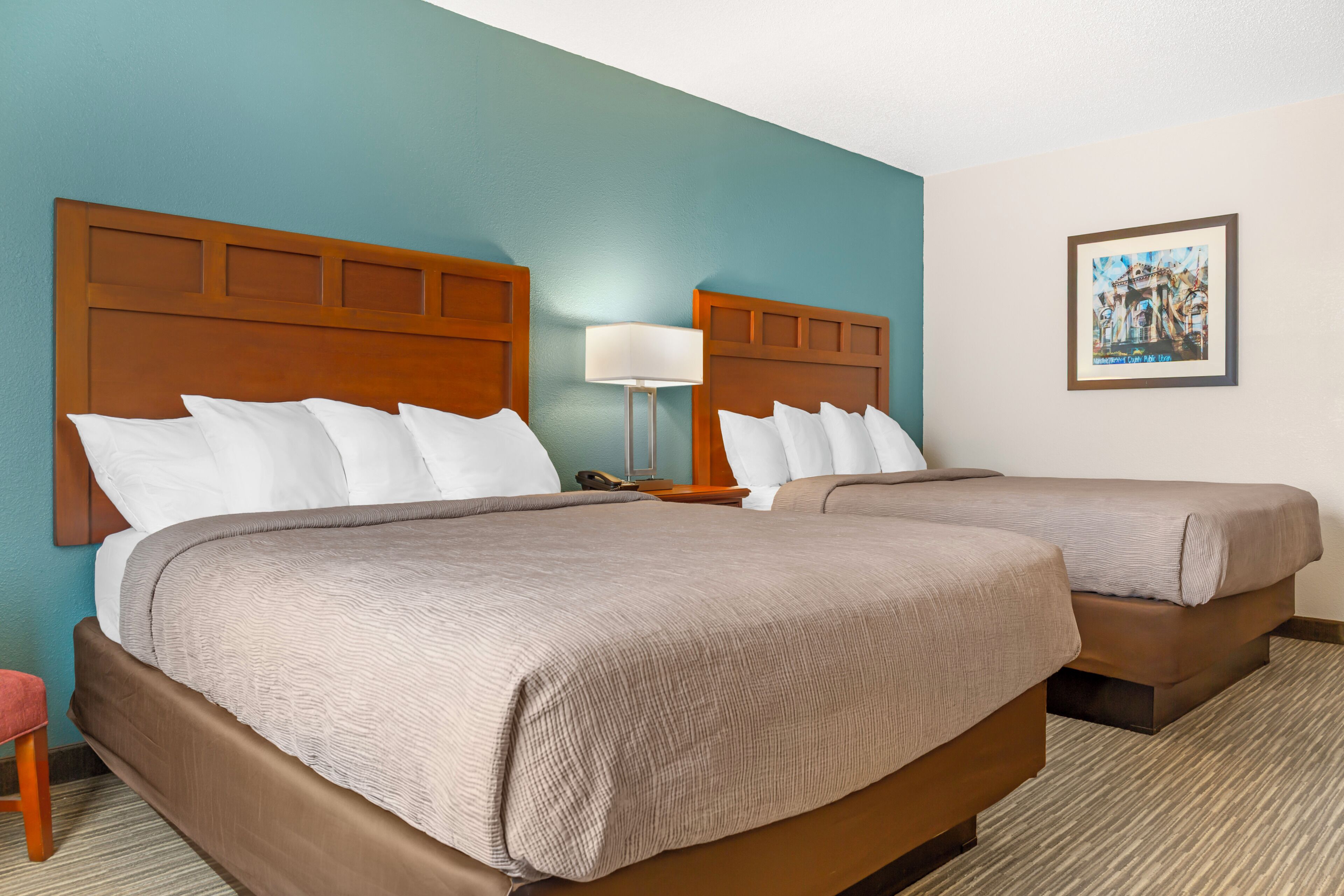 A hotel room with two beds, a nightstand, a lamp, and a framed picture on the wall.