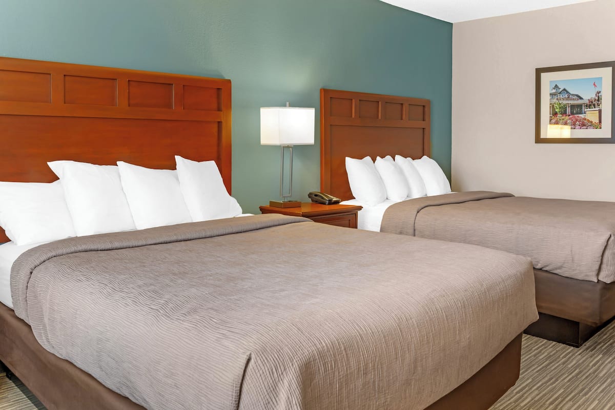 A hotel room with two beds, a nightstand, a lamp, and a framed picture on the wall.