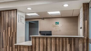 A reception desk with a wooden finish, a Dell computer, and a sign indicating check-in times. - Red Lion Inn & Suites Bucyrus North (Bucyrus)