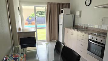 A compact kitchen with a refrigerator, microwave, stove, and sink. There's a dining table with chairs and a view of a pool outside.