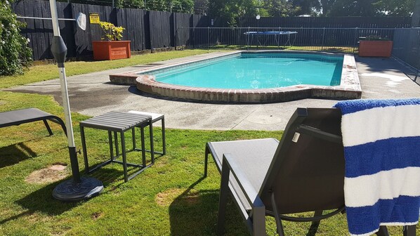 A rectangular swimming pool with a brick border, surrounded by a grassy lawn and a wooden fence. - Aztec Motel (Palmerston North)