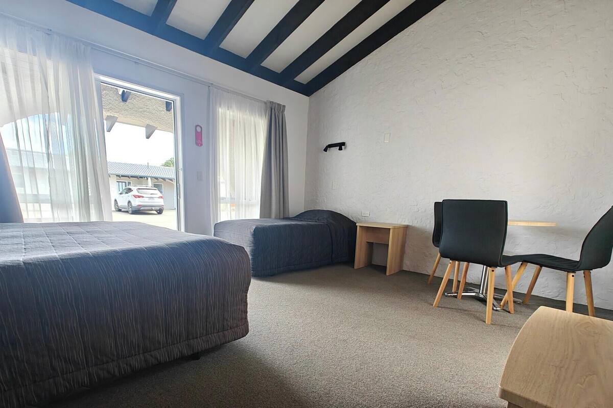A hotel room with two beds, a desk, a chair, and a view of a car outside.