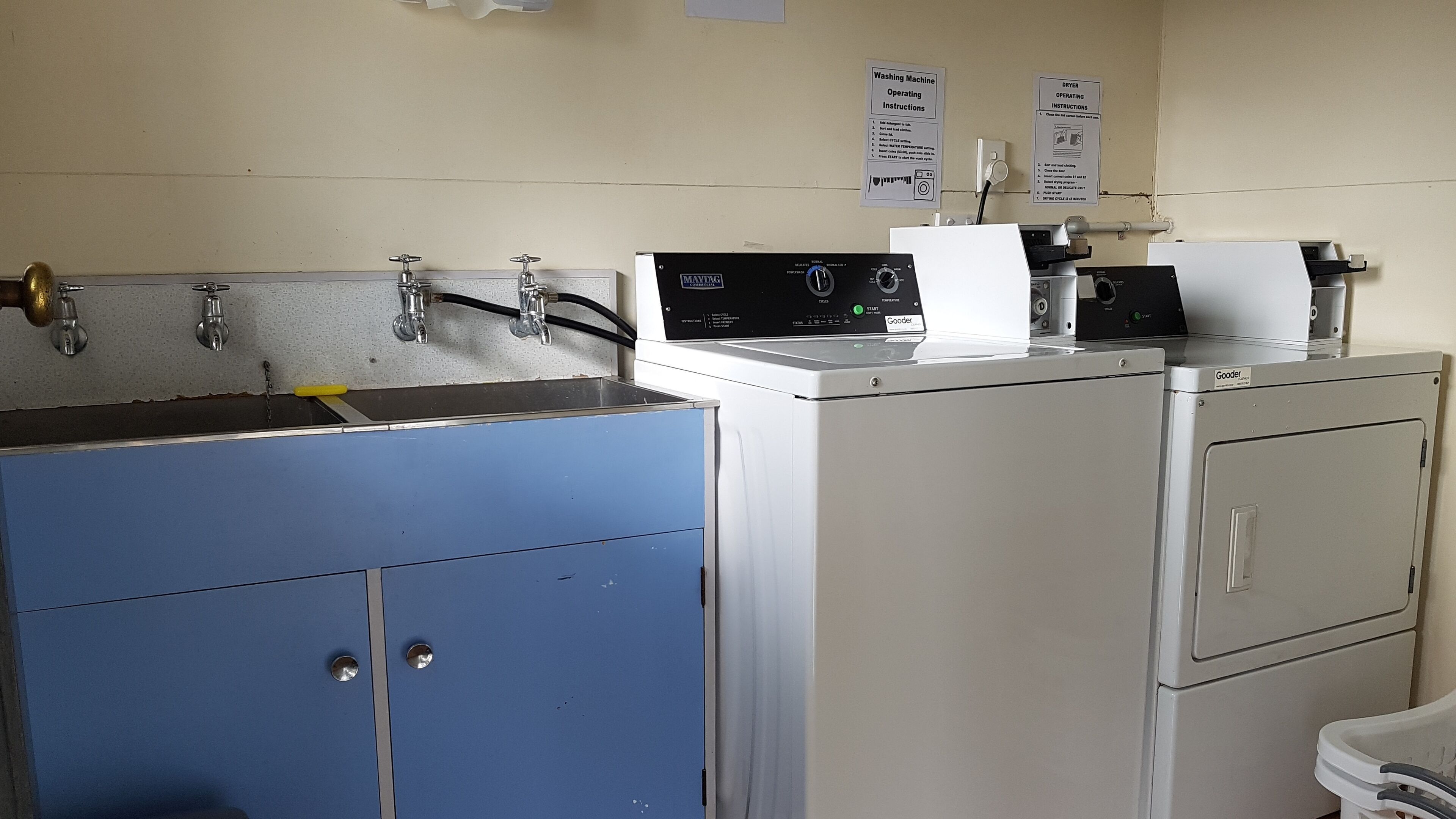 A laundry room with a blue cabinet, a white washing machine, and a dryer. There are operating instructions on the wall.