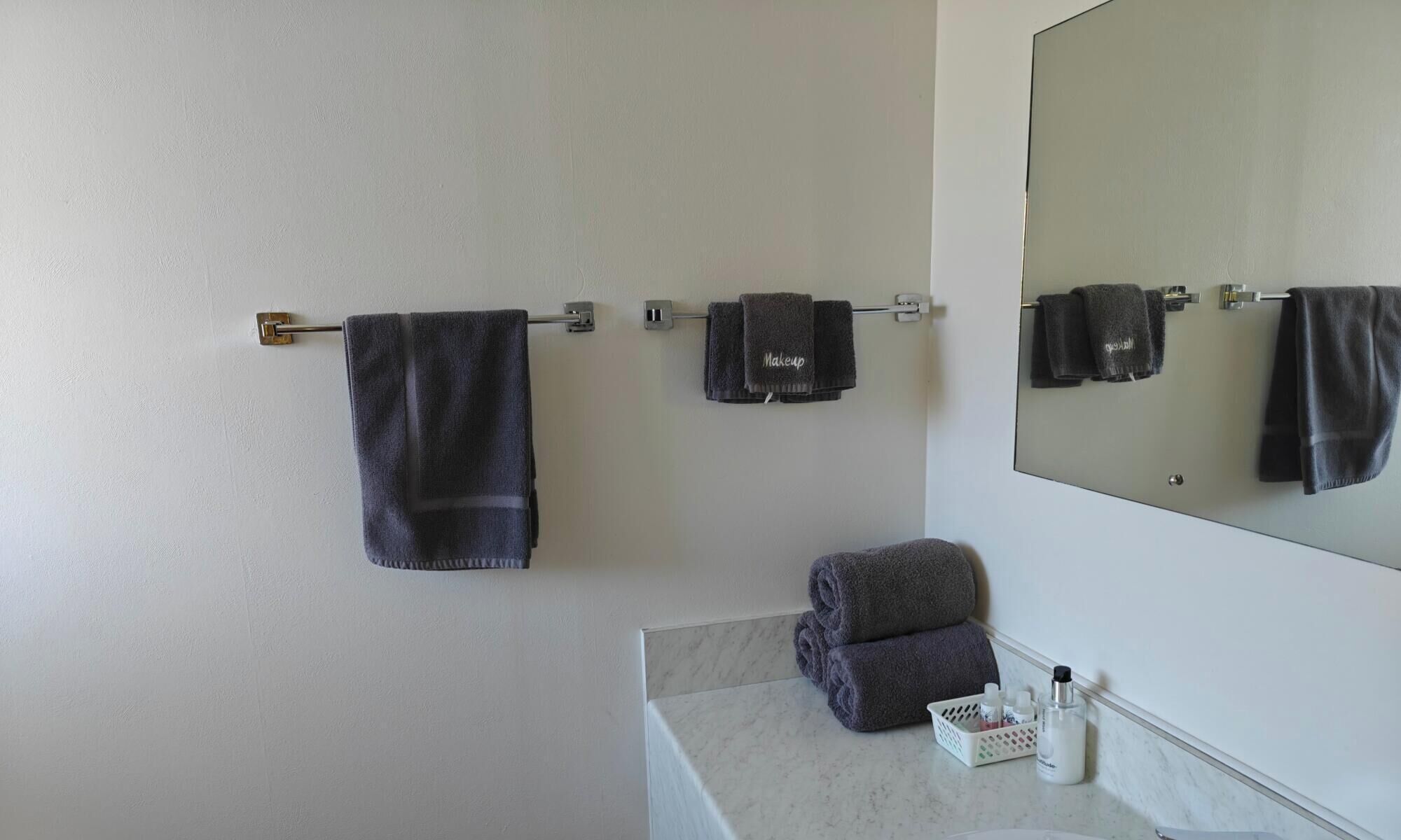 A bathroom with a towel rack holding three towels, a mirror, and a sink area with toiletries.