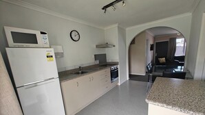 Una cocina moderna con microondas, estufa y lavaplatos. Hay un reloj en la pared y un pequeño comedor con una mesa y sillas.