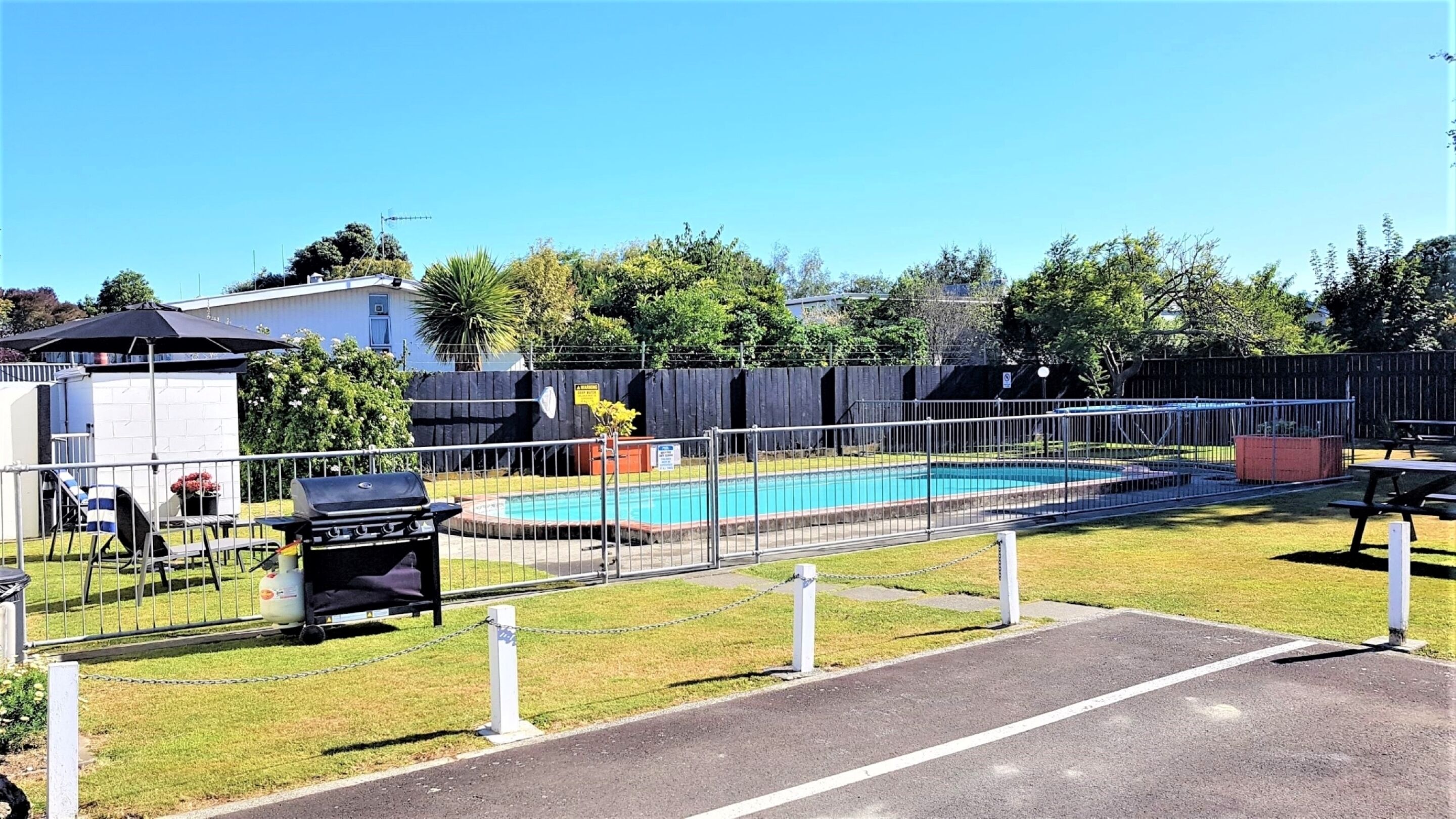 Une cour arrière clôturée avec une piscine, un barbecue et une table de pique-nique.
