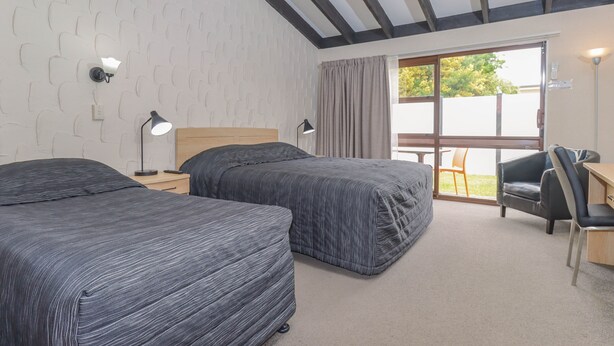 Habitación de hotel con dos camas, un escritorio, una silla y un ventanal grande con cortinas.