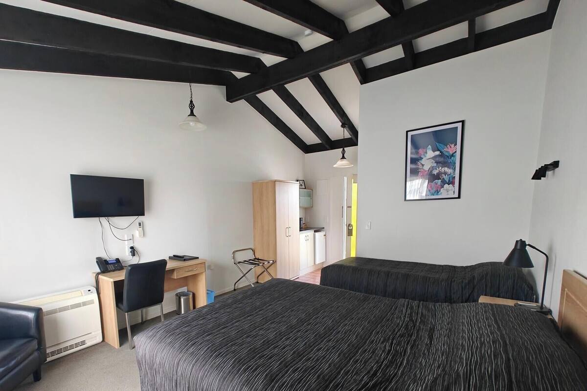 A hotel room with a bed, a desk, a chair, a TV, a wardrobe, and a painting.