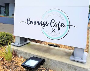 A sign for 'Cravings Cafe' with a circular logo and a stylized 'X' symbol. - Aztec Motel (Palmerston North)