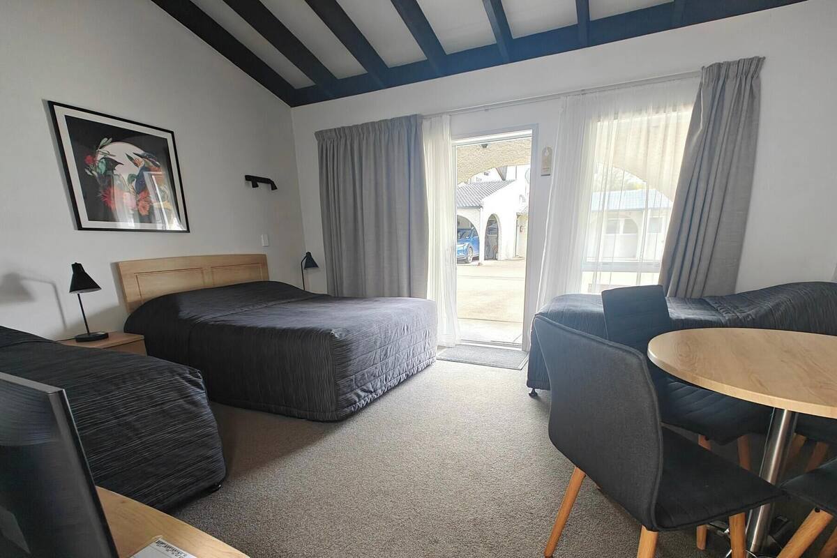 A hotel room with a bed, a sofa, a small table, and a desk. There is a window with curtains, a picture on the wall, and a view of the outside.