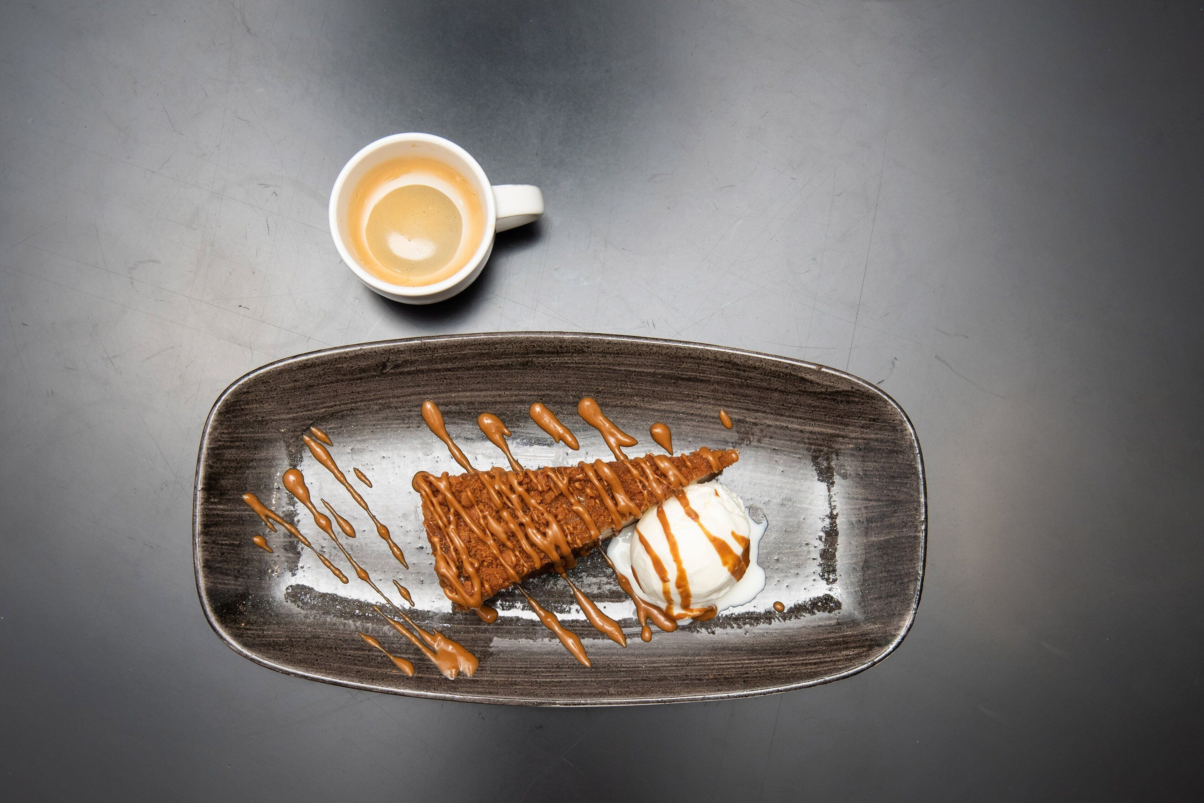 A dessert plate with a brownie and ice cream, and a cup of coffee on a dark surface.