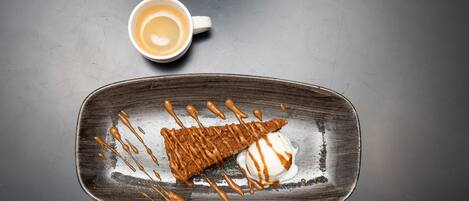 A dessert plate with a brownie and ice cream, and a cup of coffee on a dark surface.