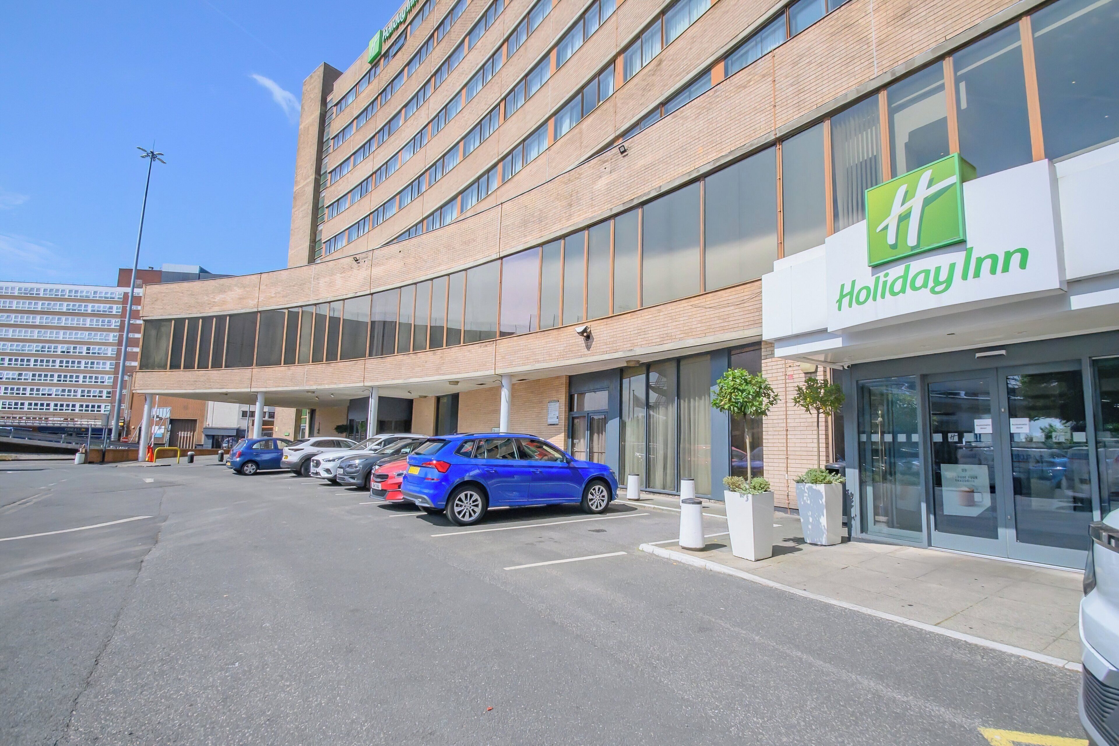 A Holiday Inn hotel with a parking lot and several cars parked in front.