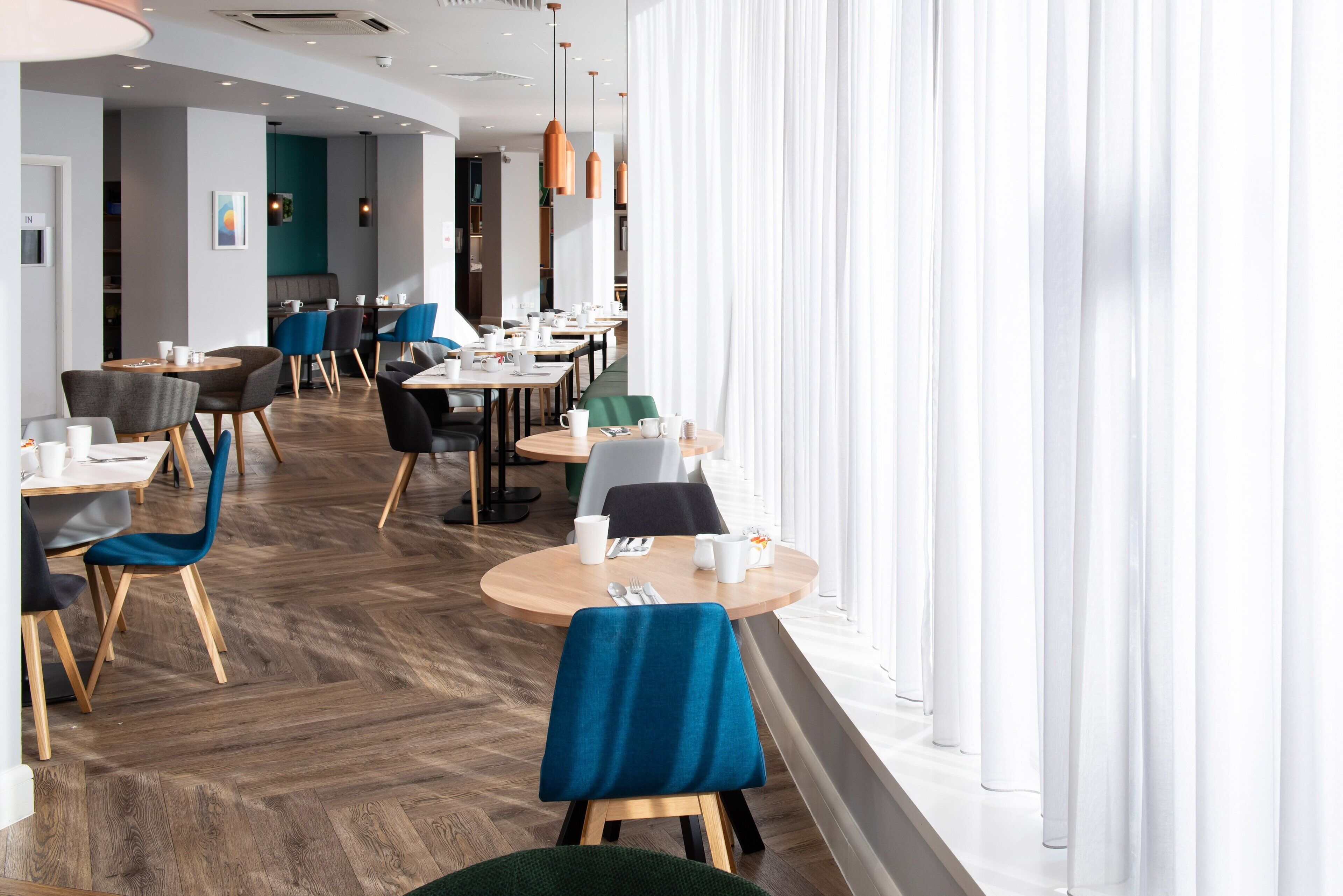 Un área de comedor moderna con mesas redondas, sillas e iluminación colgante.