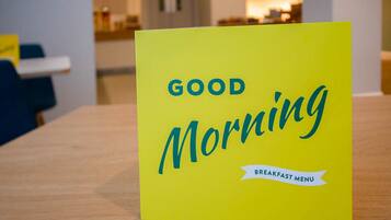 A bright yellow sign with the text "GOOD MORNING" and "BREAKFAST MENU" on a wooden table in a room.