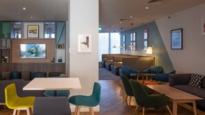 A modern hotel lobby with a seating area, a television, and a dining space.