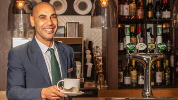 Zona de bar con una persona sosteniendo una taza, un grifo de cerveza y estantes con botellas.
