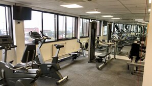 A gym with cardio machines, weight equipment, and large windows offering city views.