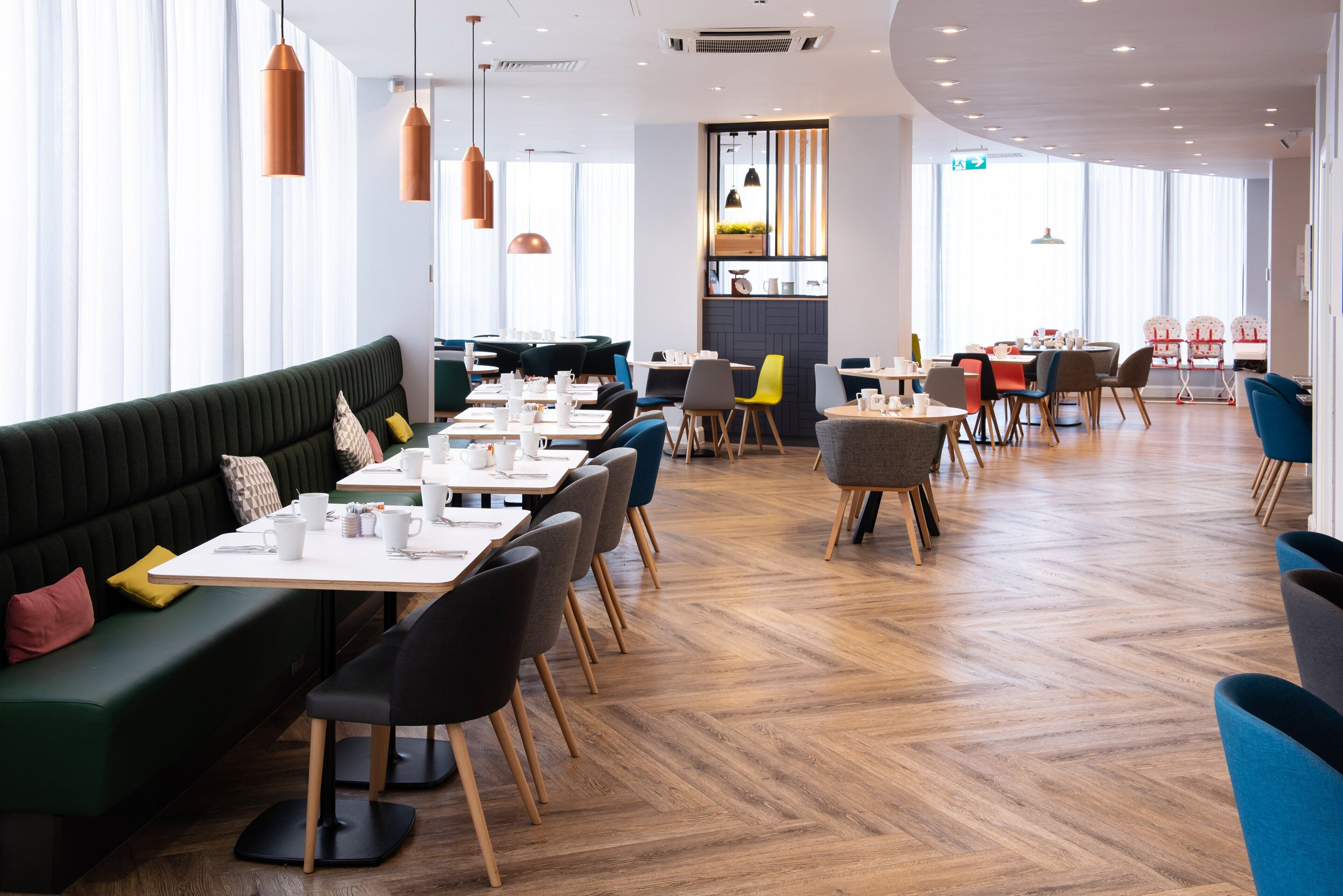Un restaurante moderno con un sofá verde, varias mesas y sillas.