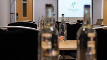 A conference room with a projector screen displaying a presentation, a wooden table with several bottles, and a laptop.