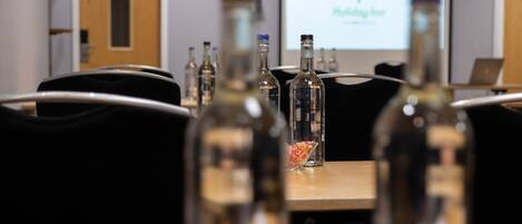 A conference room with a projector screen displaying a presentation, a wooden table with several bottles, and a laptop.