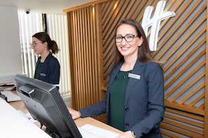 A reception desk with a computer monitor, a keyboard, and a name tag. - Holiday Inn Preston by IHG (Preston)