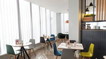 A modern dining area with round tables and chairs, large windows with sheer curtains, and a black brick accent wall with pendant lighting.