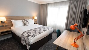 A hotel room with a large bed, a desk, a chair, a TV, and curtains.