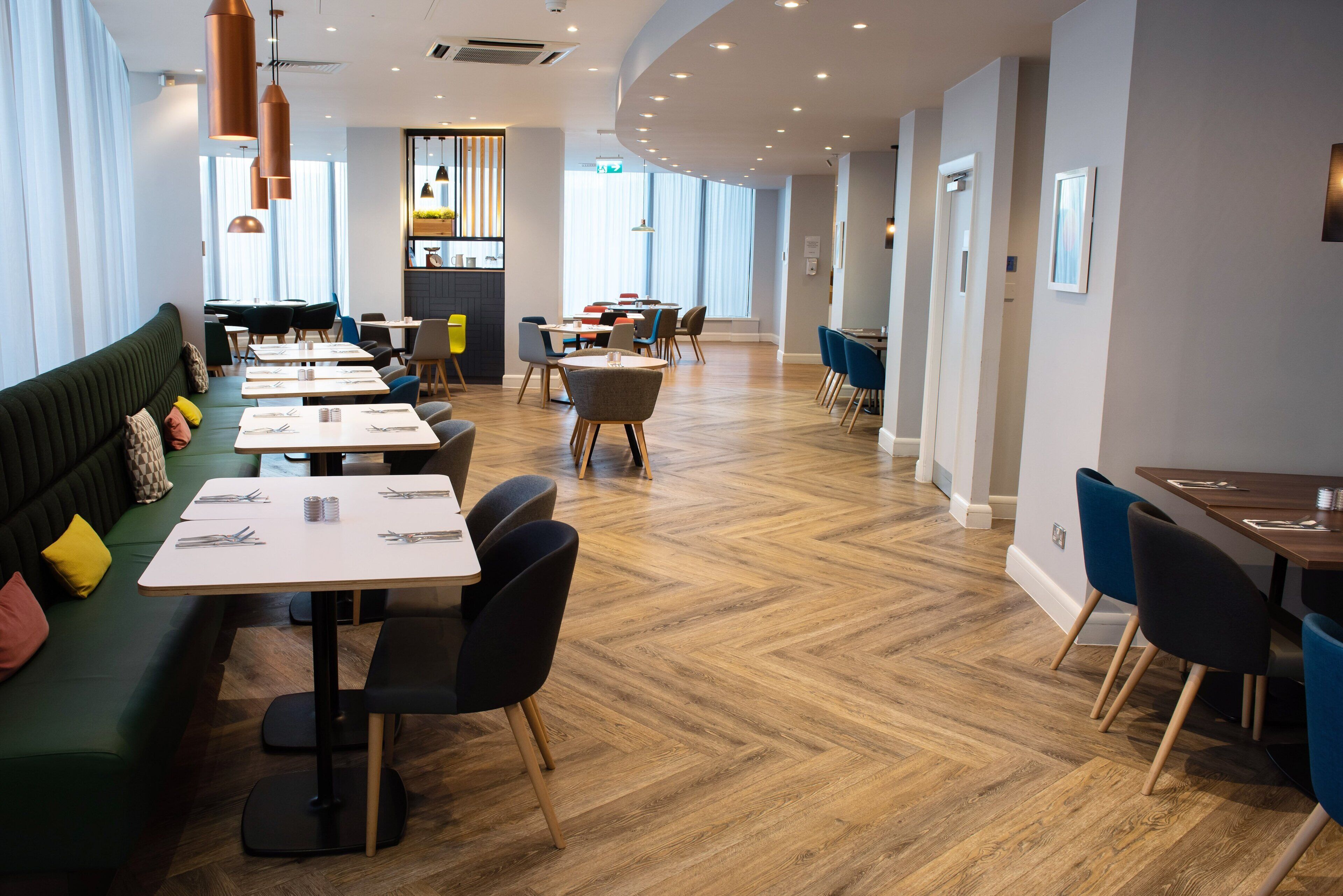 Un restaurante moderno con suelo de madera, asientos verdes y sillas azules.