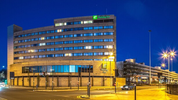 A Holiday Inn hotel with multiple floors, a parking garage, and a street view at night.