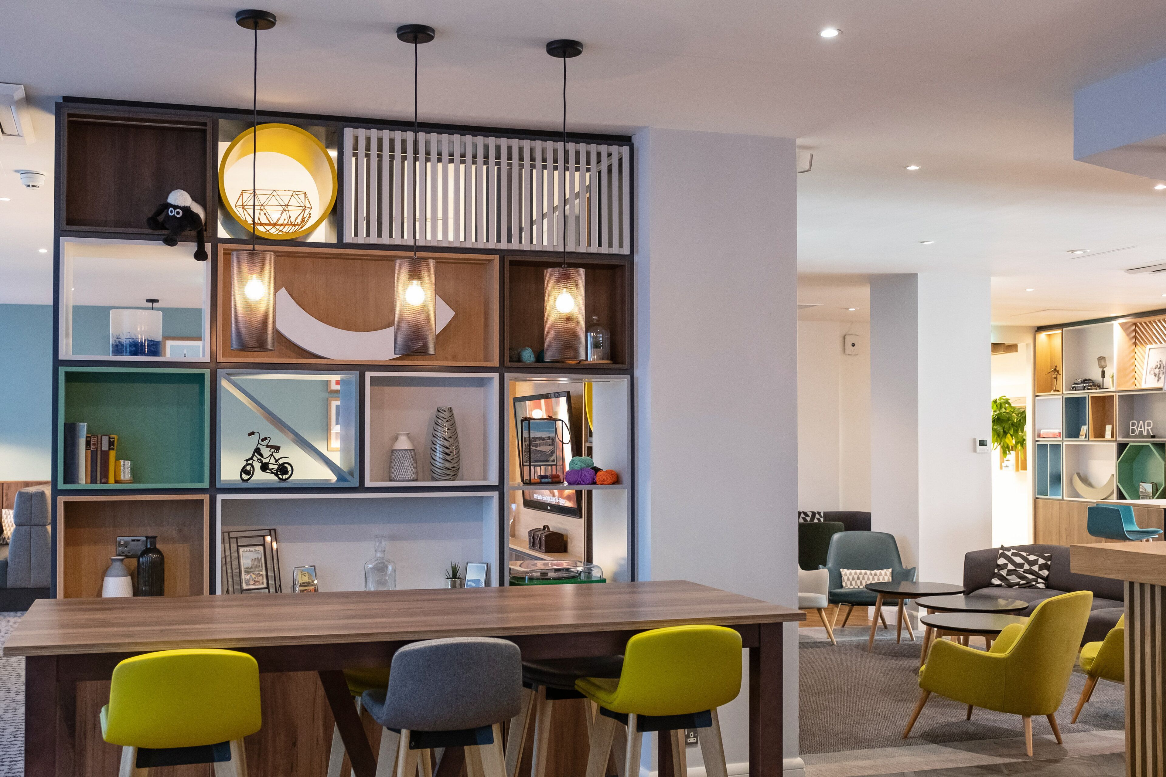 A modern interior with a wooden dining table, yellow and gray chairs, and a variety of shelves with decorative items.