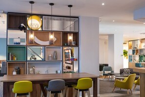 A modern interior with a wooden dining table, yellow and gray chairs, and a variety of shelves with decorative items. - Holiday Inn Preston by IHG (Preston)