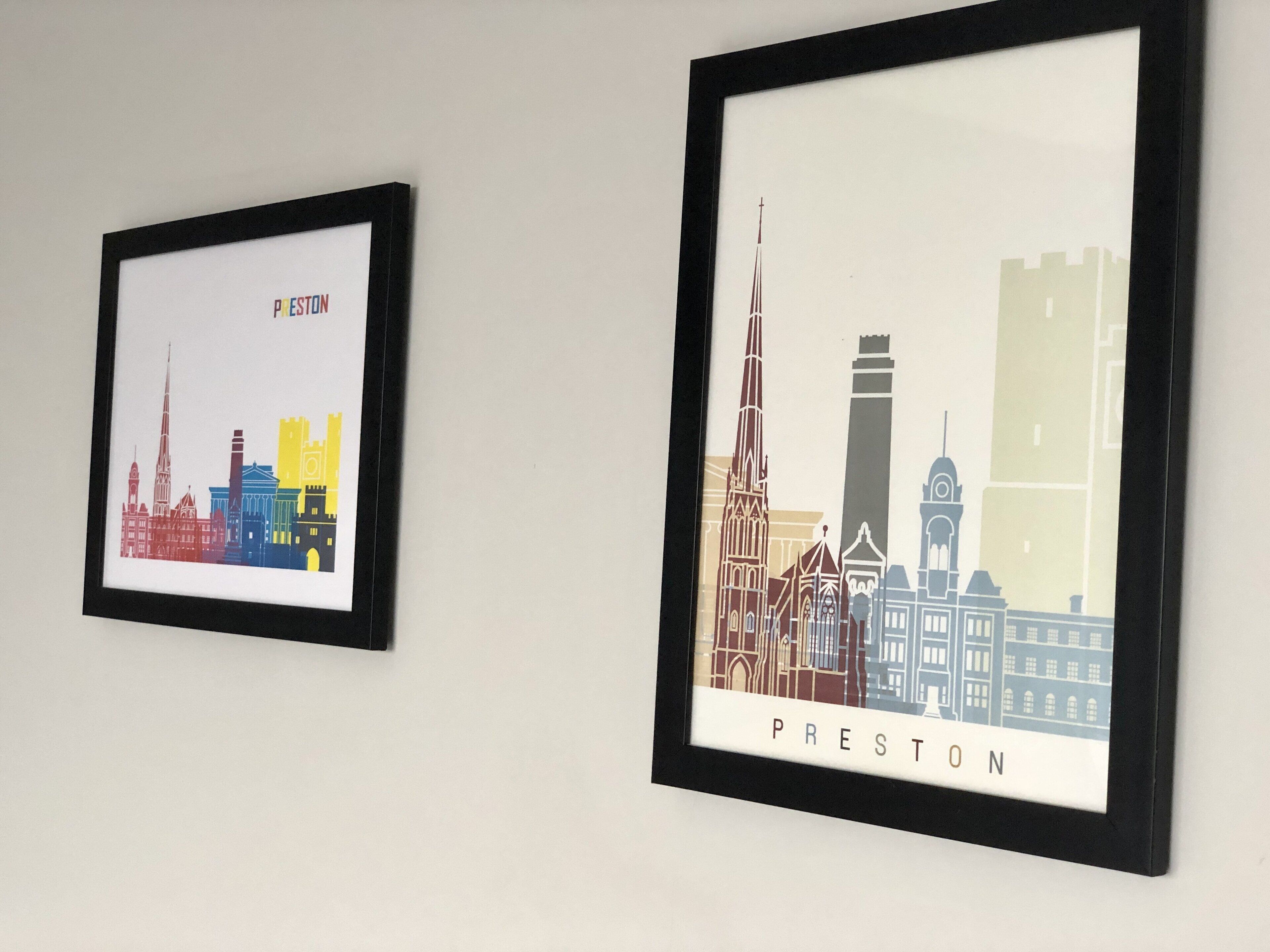 Dos obras de arte con paisajes urbanos enmarcados, etiquetadas como 'PRESTON', sobre una pared lisa.