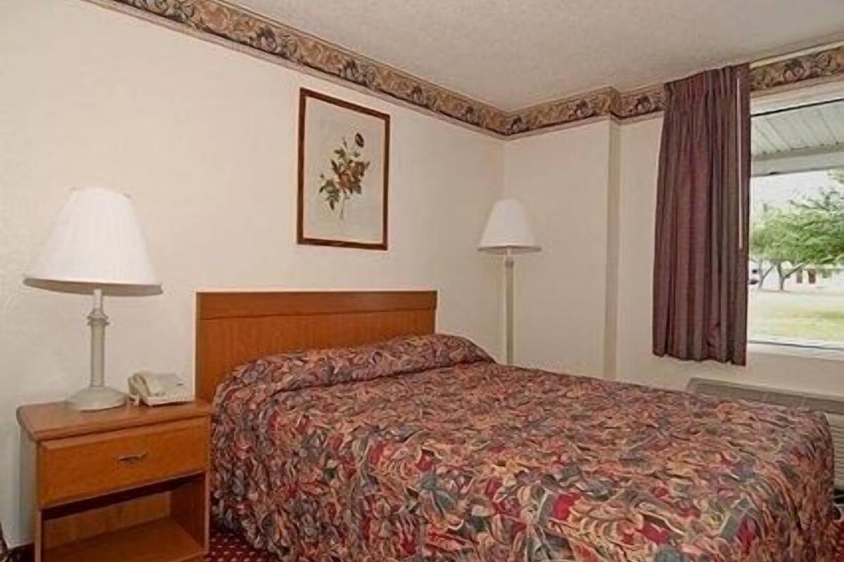 A hotel room with a bed, bedside lamps, a nightstand, a framed picture on the wall, and a window with curtains.