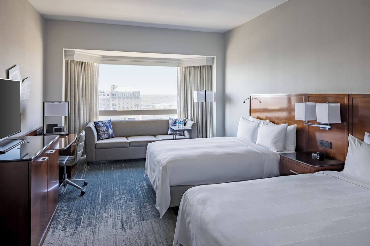A hotel room with two beds, a desk, a chair, a TV, and a window with curtains.