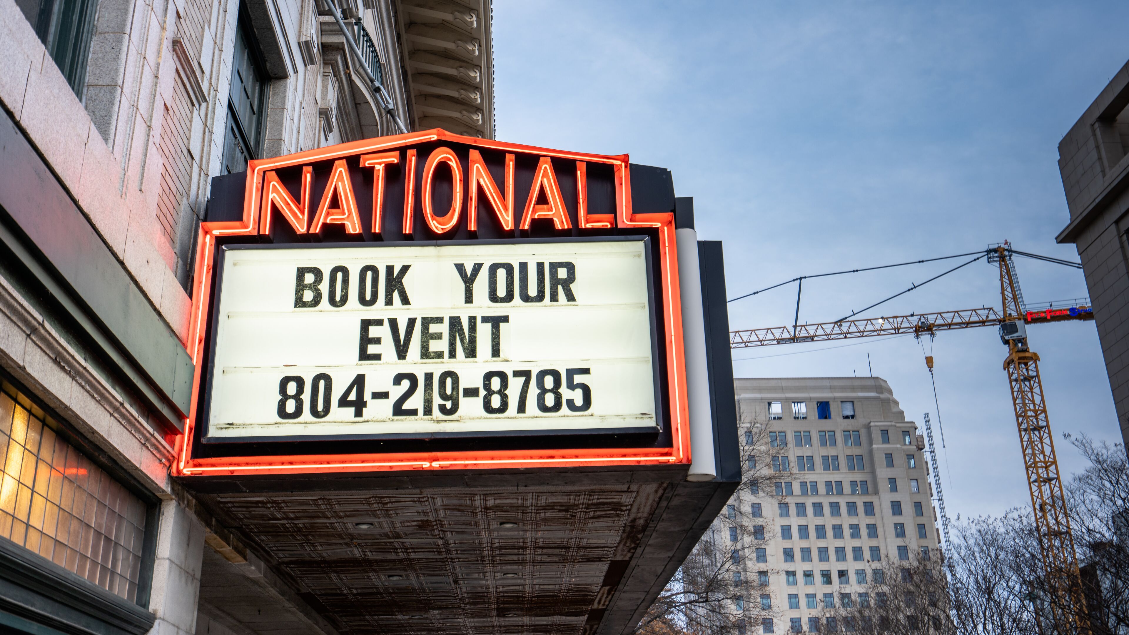 A neon sign advertising a booking service for events with a phone number.