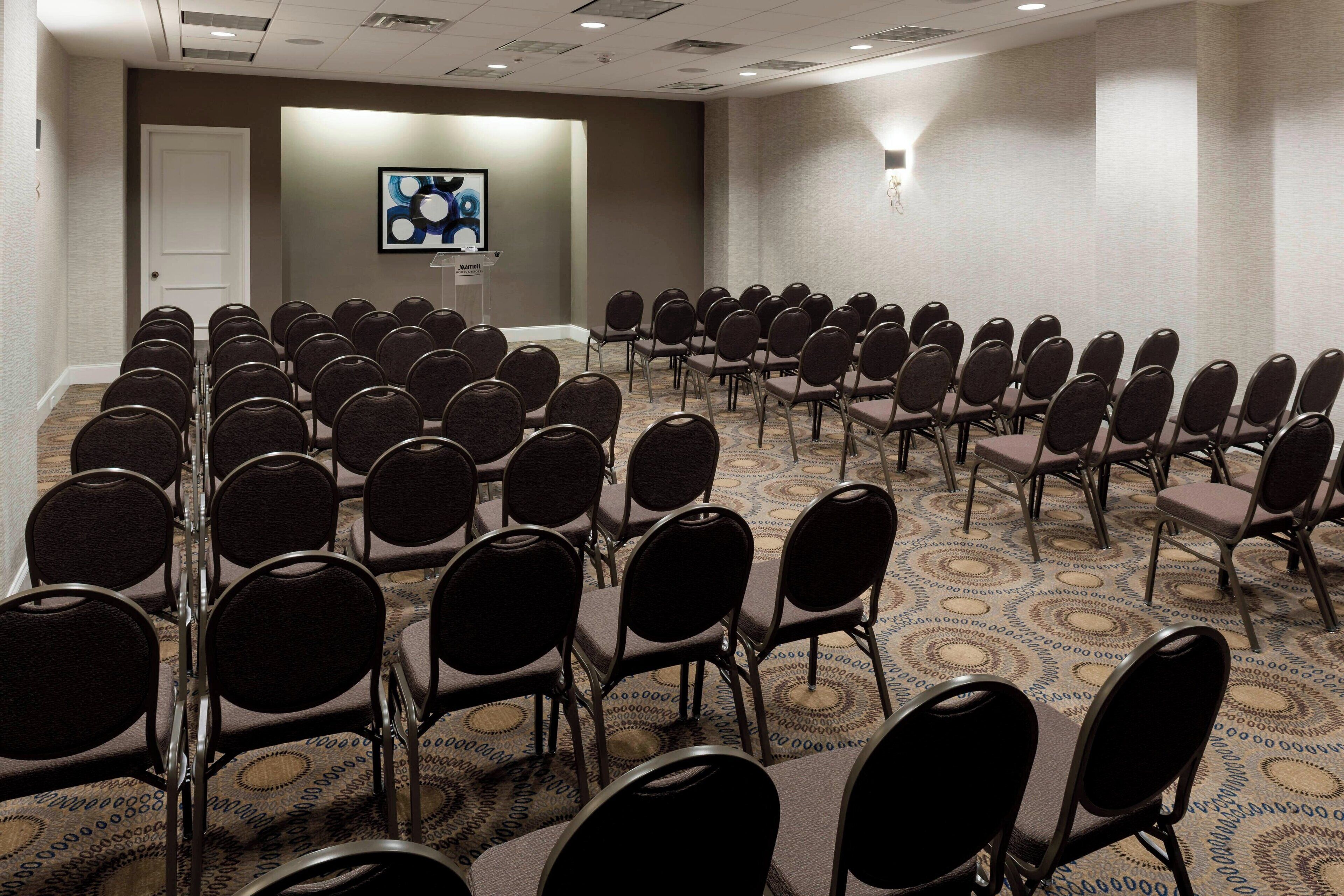 A conference room with rows of chairs, a podium, and a screen on the wall.