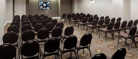 A conference room with rows of chairs, a podium, and a screen on the wall.