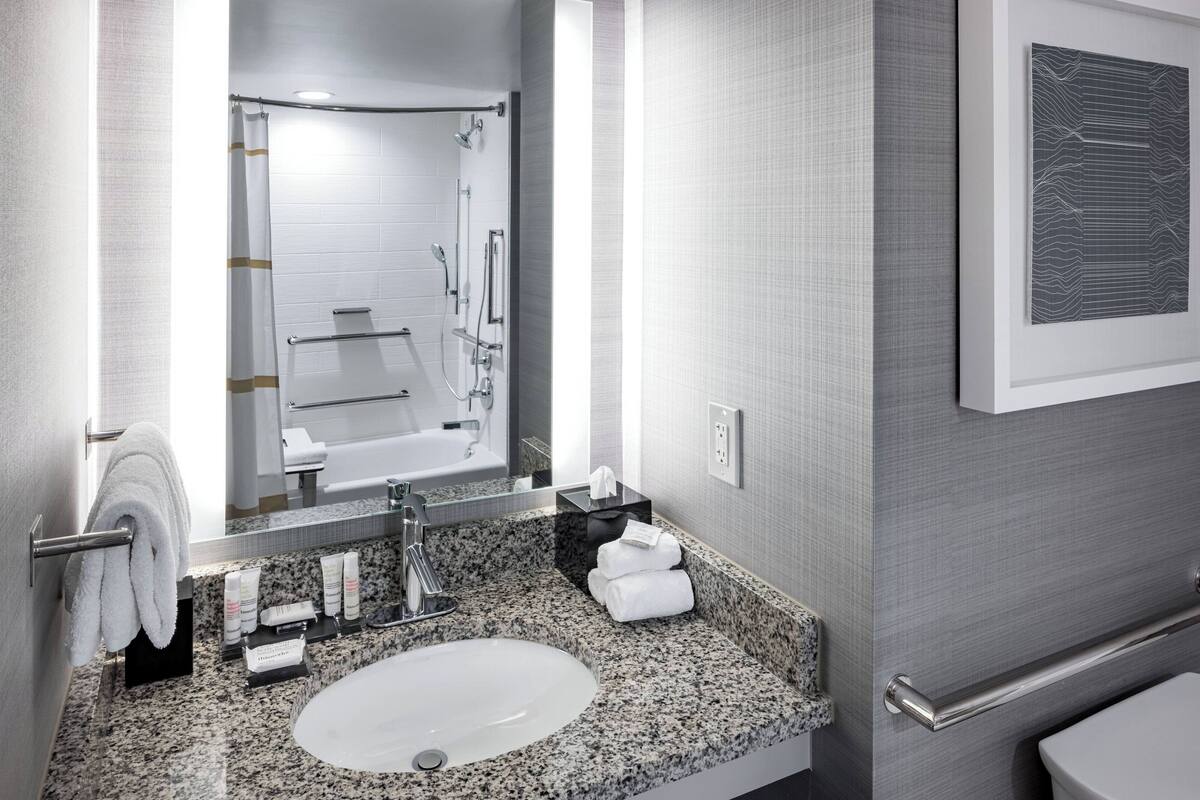A modern bathroom with a granite countertop, a white sink, a glass shower enclosure, and a framed artwork on the wall.