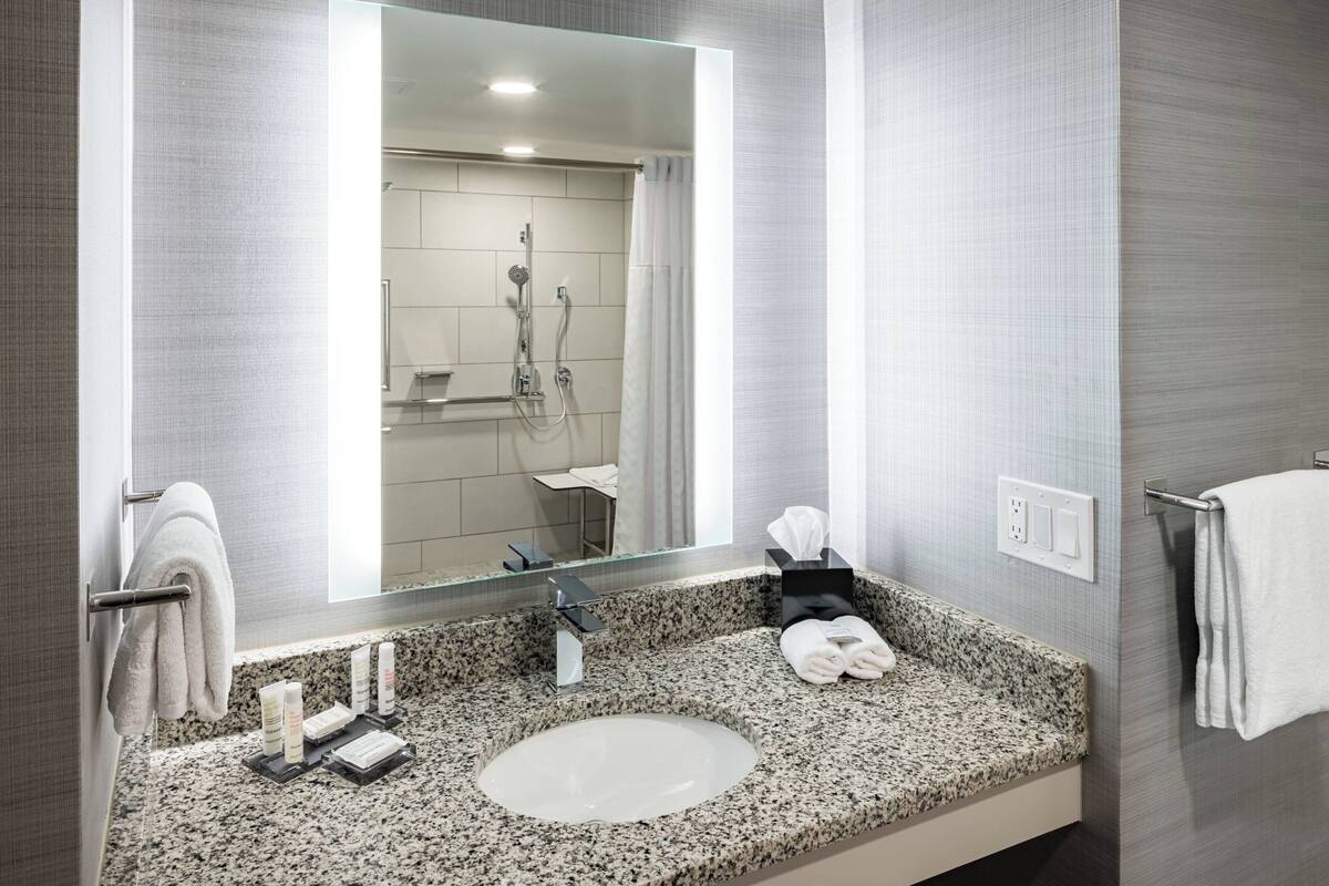 A modern bathroom with a granite countertop, a large mirror, a sink, and a shower area.