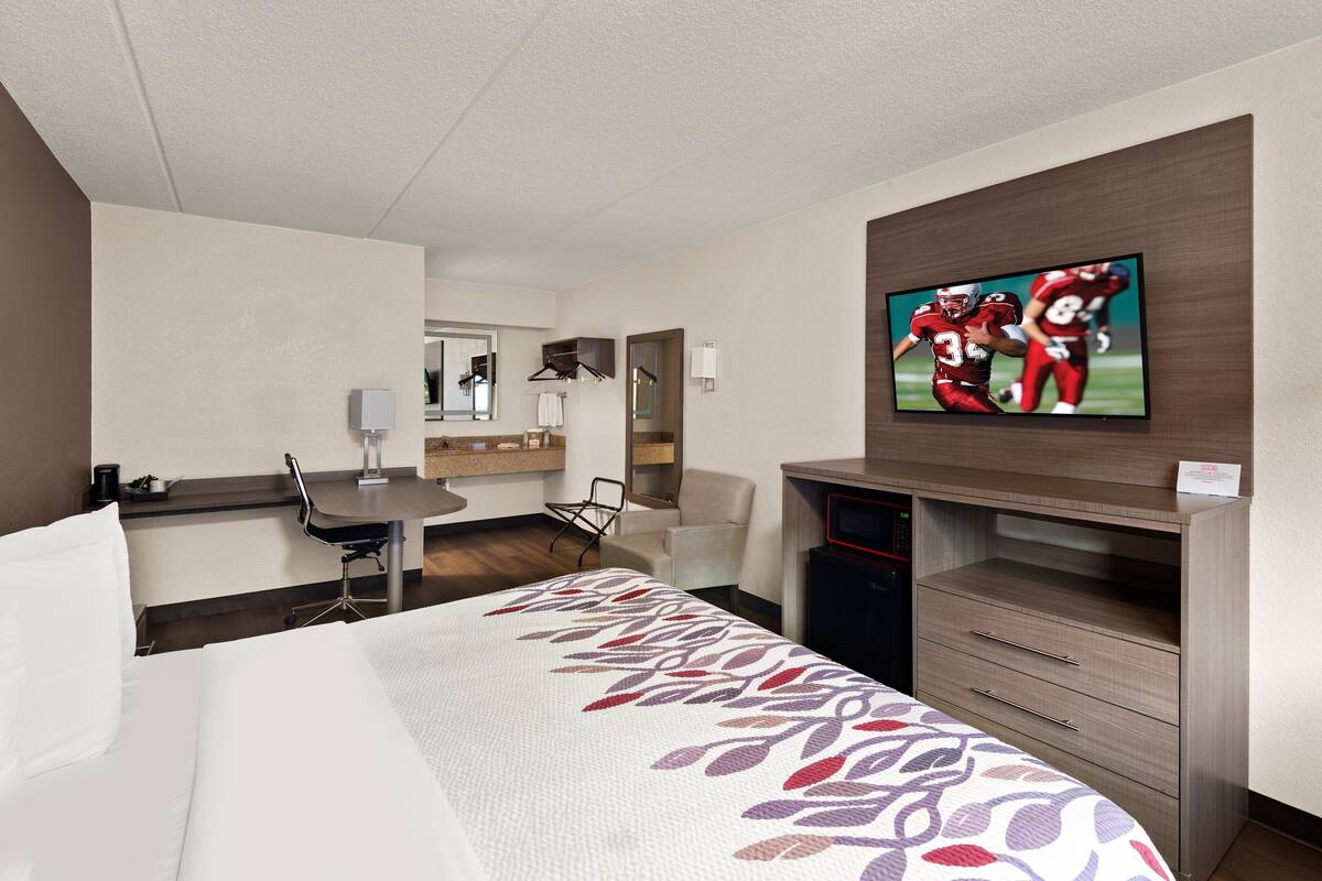 Een hotelkamer met een bed, een bureau, een stoel, een televisie en een dressoir.