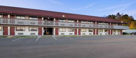 A multi-story motel with a flat roof, a covered parking area, and a clear sky.