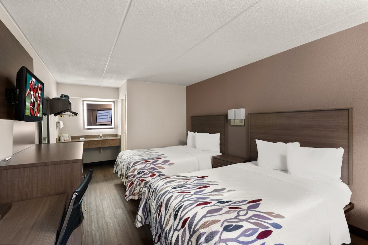 Een hotelkamer met twee bedden, een bureau, een televisie en een raam.
