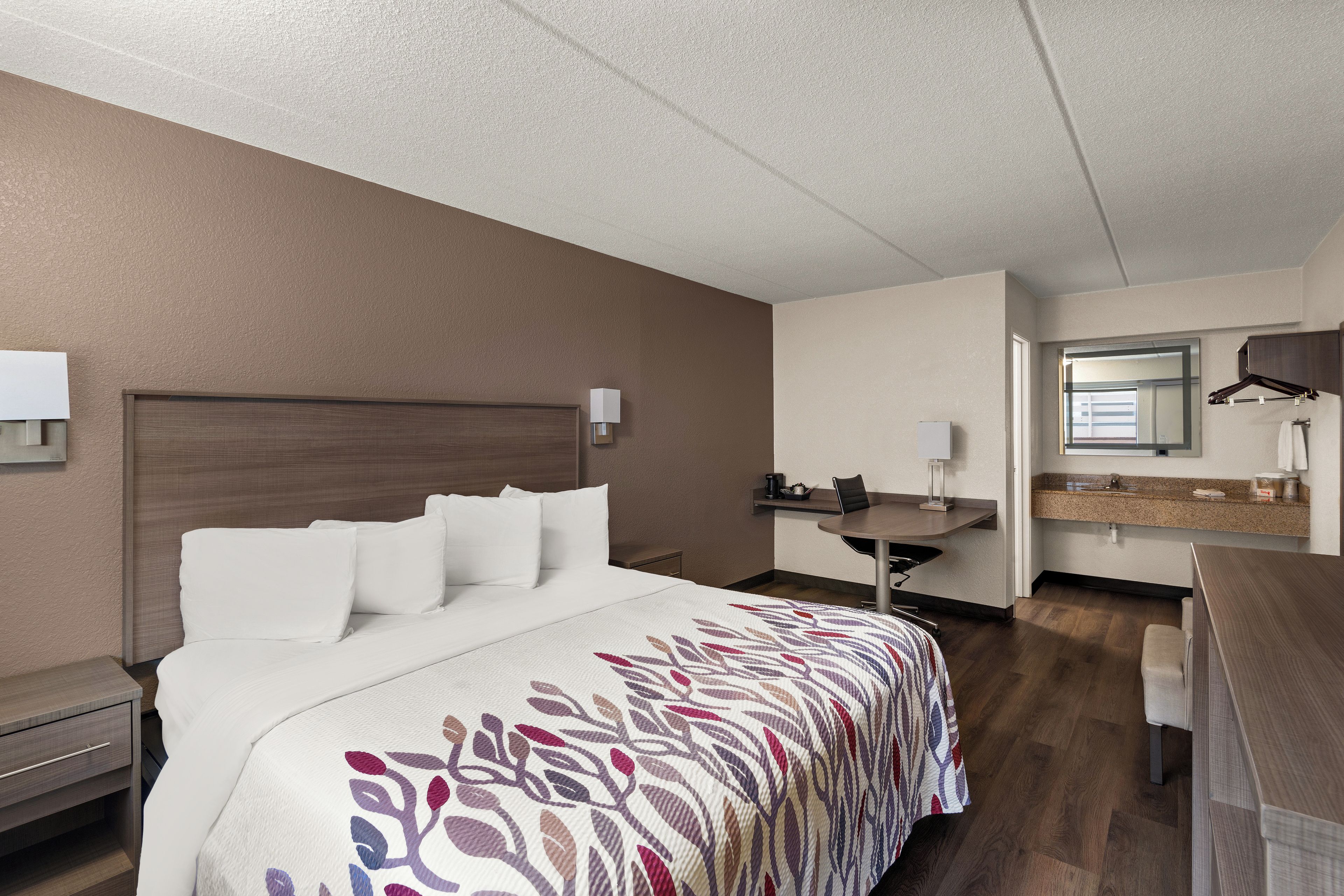 A hotel room with a bed, a desk, a chair, and a bathroom.