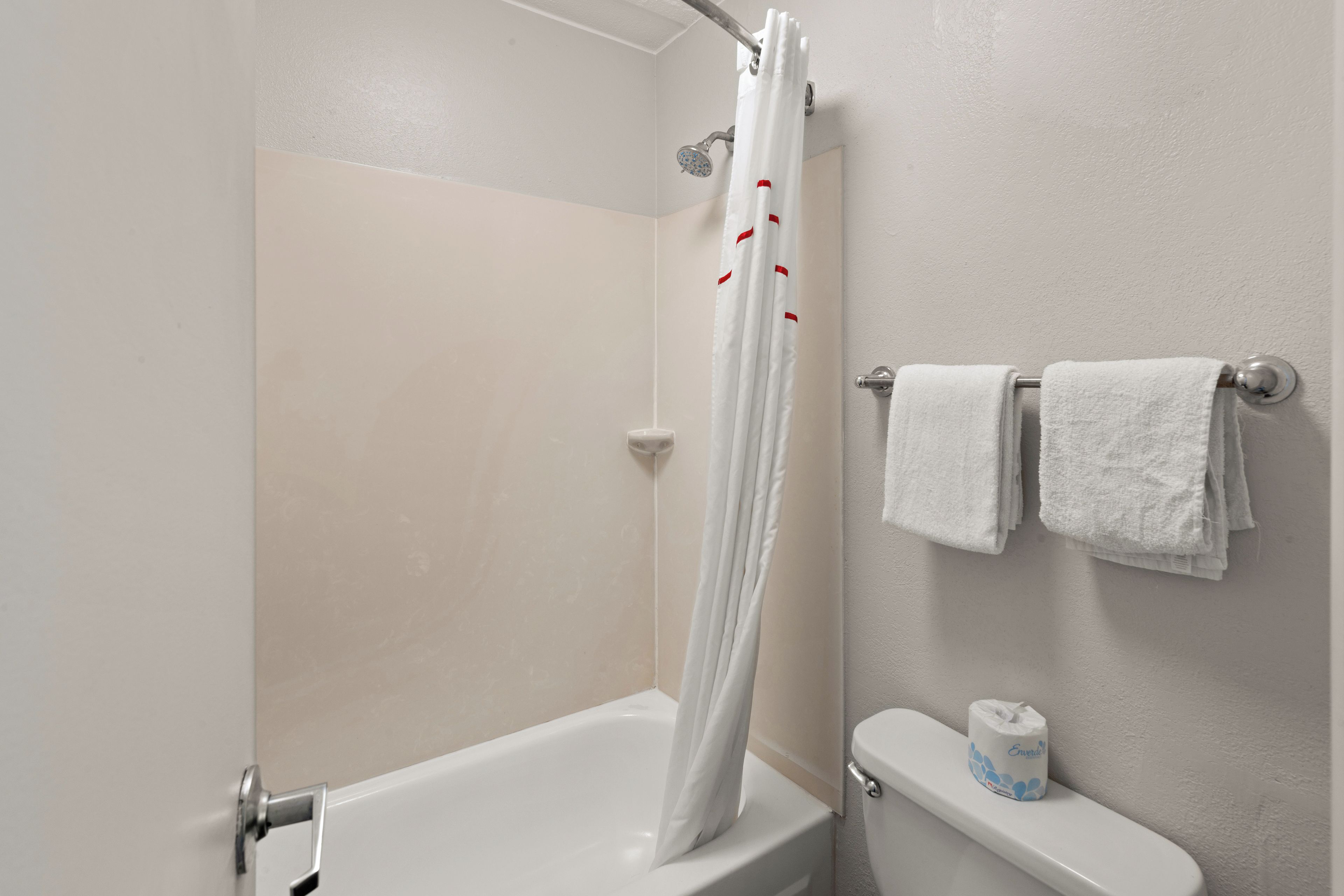 A bathroom with a shower curtain, a toilet, and a stack of white towels.